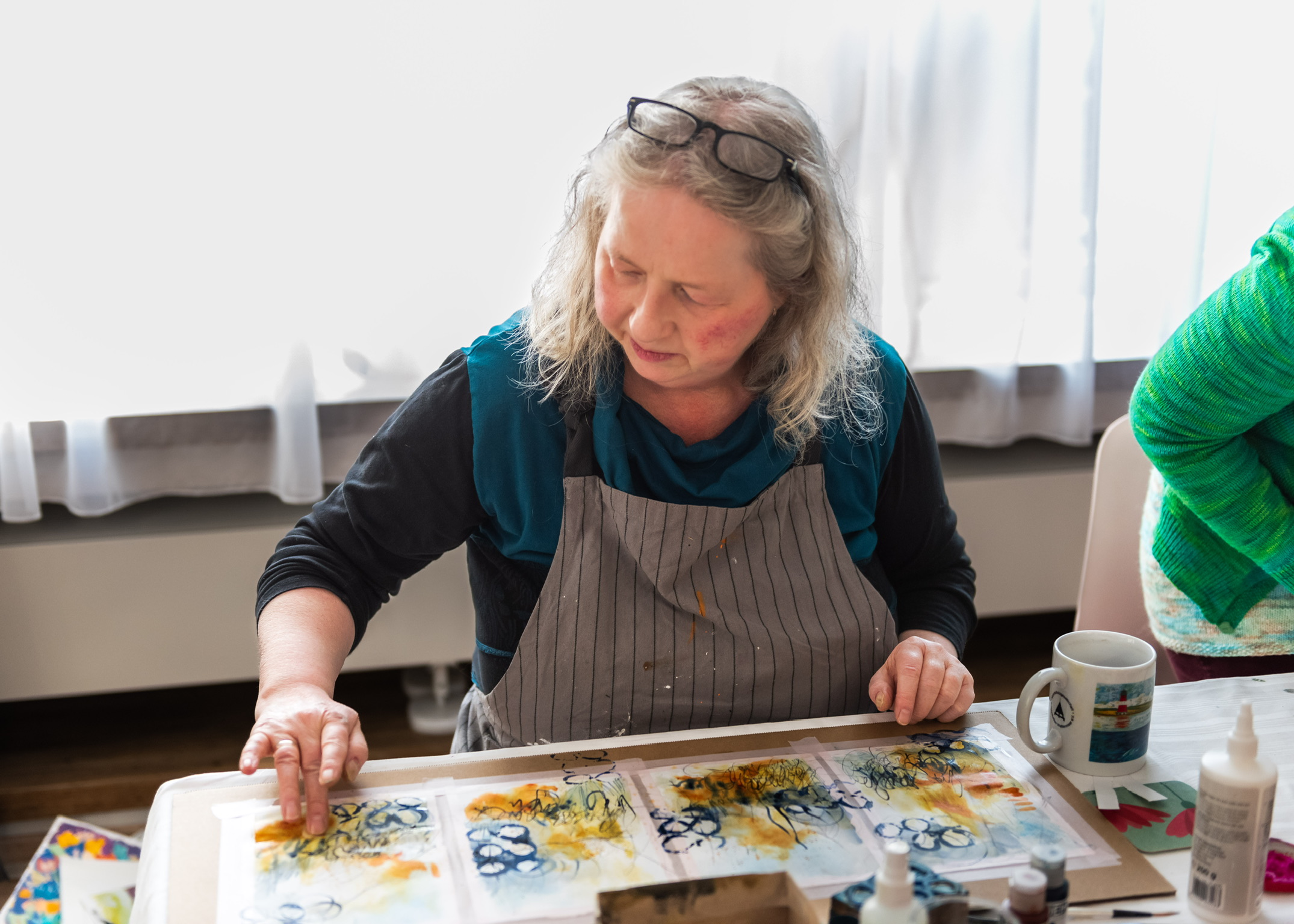 Andrea Gunkler in her bright art studio holding a paintbrush during a creative healing session